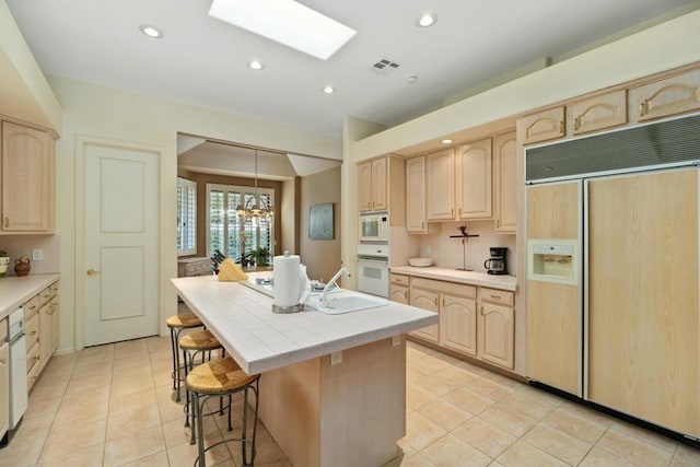 kitchen featuring sink, light brown cabinets, built in appliances, a kitchen island, and light tile patterned flooring