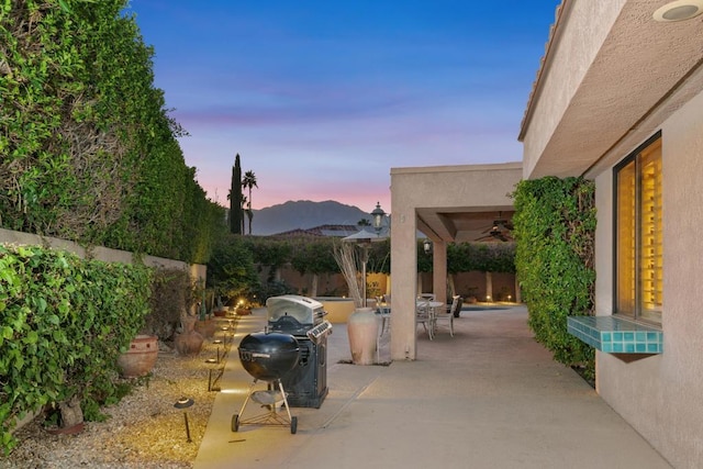 patio terrace at dusk with ceiling fan, a mountain view, and grilling area