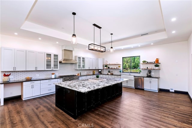 kitchen featuring a large island, stainless steel appliances, wall chimney range hood, decorative light fixtures, and a tray ceiling