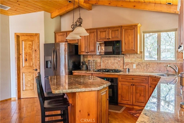 kitchen featuring a center island, black appliances, sink, light stone countertops, and tasteful backsplash