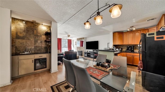 kitchen with decorative light fixtures, wine cooler, black fridge, light wood-type flooring, and ceiling fan