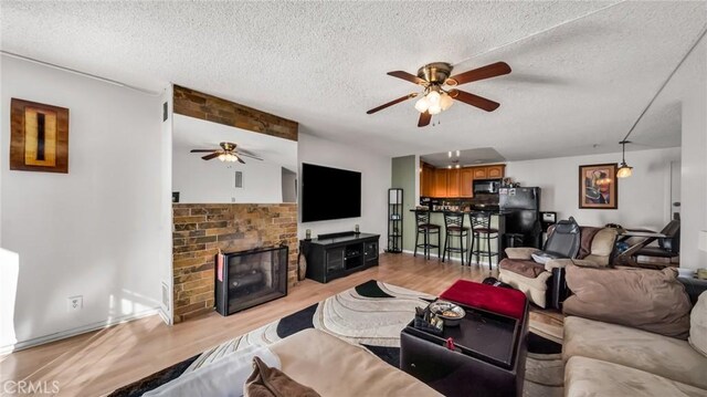 living room featuring a fireplace, a textured ceiling, ceiling fan, and light wood-type flooring