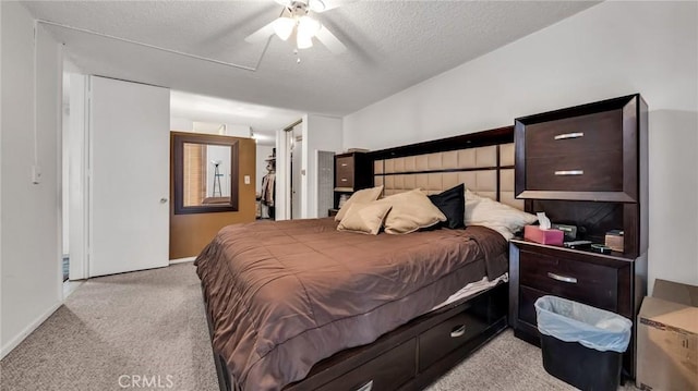 bedroom featuring a textured ceiling, light colored carpet, a ceiling fan, a closet, and a walk in closet