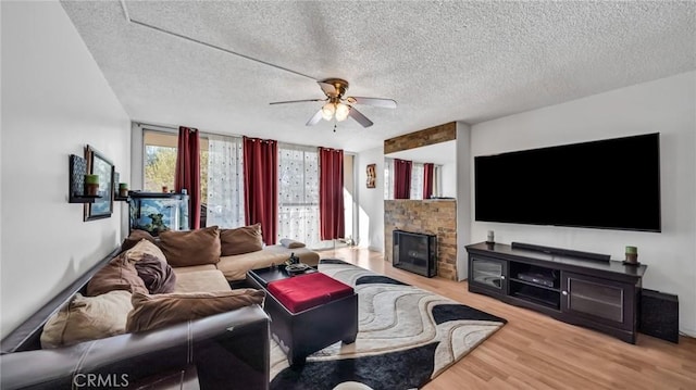 living room featuring ceiling fan, a fireplace, floor to ceiling windows, light hardwood / wood-style flooring, and a textured ceiling