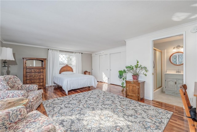 bedroom featuring ornamental molding, multiple closets, ensuite bathroom, and wood finished floors