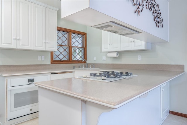 kitchen featuring a peninsula, white appliances, a sink, white cabinets, and light countertops