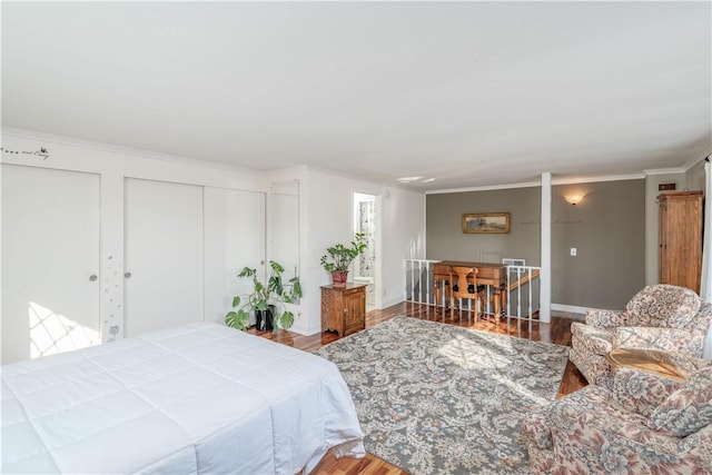 bedroom featuring ornamental molding, two closets, baseboards, and wood finished floors