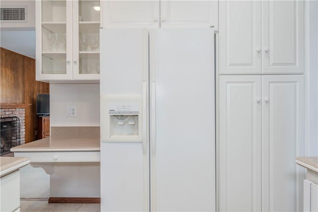 kitchen featuring visible vents, glass insert cabinets, a brick fireplace, white fridge with ice dispenser, and white cabinetry