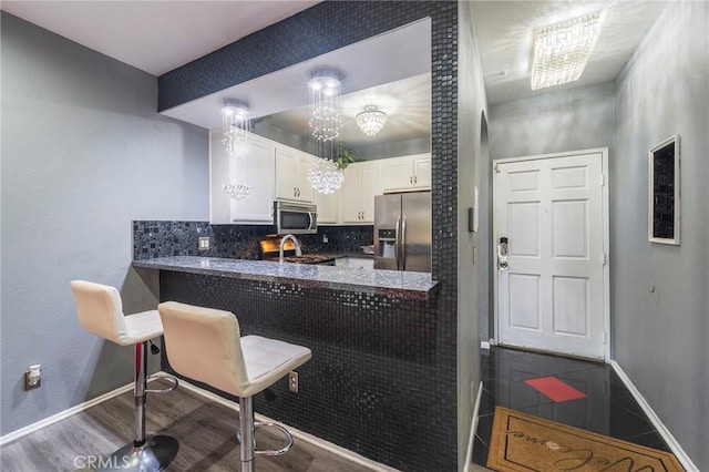 kitchen with white cabinetry, tasteful backsplash, appliances with stainless steel finishes, kitchen peninsula, and hardwood / wood-style flooring