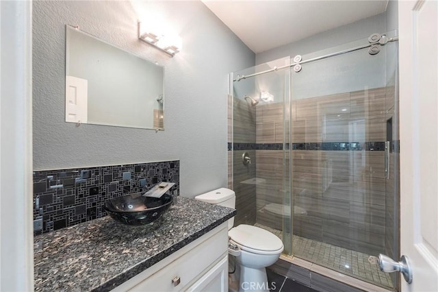 bathroom with tile patterned floors, toilet, a shower with shower door, tasteful backsplash, and vanity