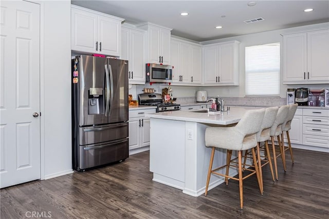 kitchen featuring dark wood-type flooring, a center island with sink, a breakfast bar area, white cabinetry, and stainless steel appliances