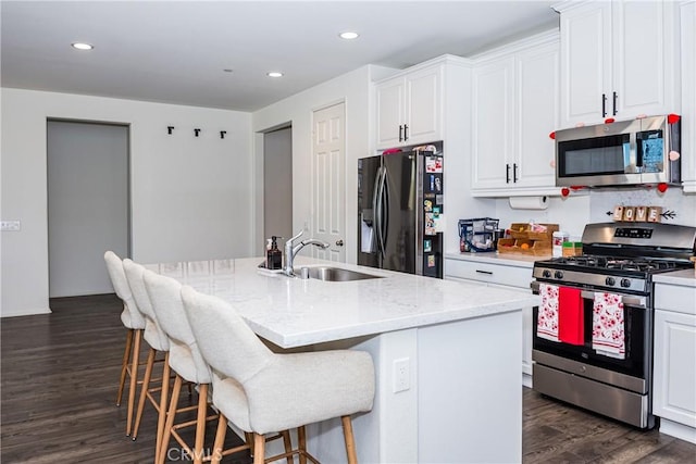 kitchen featuring light stone countertops, white cabinetry, sink, stainless steel appliances, and an island with sink