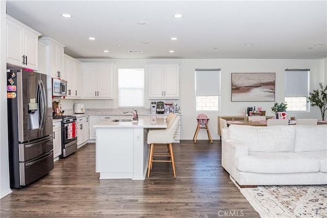 kitchen with white cabinets, a kitchen bar, stainless steel appliances, and a kitchen island with sink