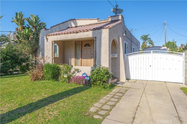 mediterranean / spanish-style home featuring a tile roof, a gate, a front lawn, and stucco siding