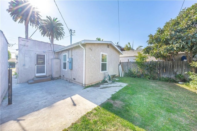 rear view of property featuring stucco siding, a lawn, a patio, and fence