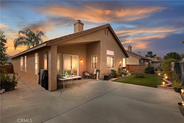 back house at dusk featuring a lawn and a patio area