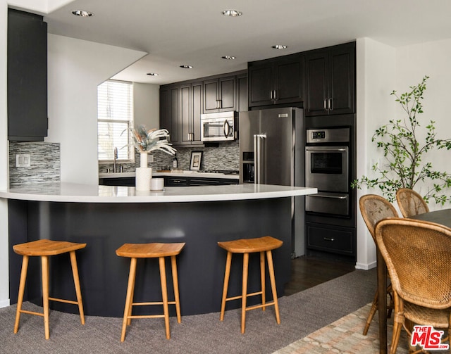 kitchen with a breakfast bar, sink, tasteful backsplash, kitchen peninsula, and stainless steel appliances