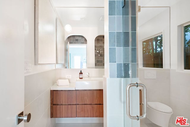 bathroom with a shower with door, vanity, tile walls, and toilet