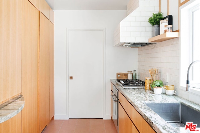 kitchen with stainless steel gas stovetop, backsplash, sink, light tile patterned floors, and light stone counters