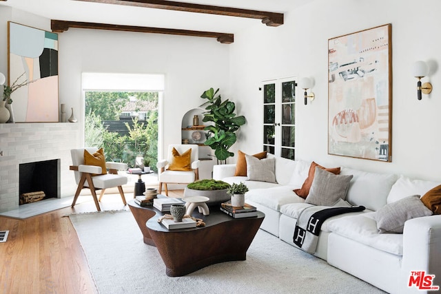 living room with beam ceiling, hardwood / wood-style flooring, and a brick fireplace