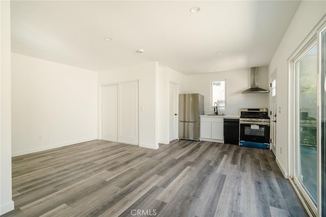 kitchen with sink, wall chimney range hood, appliances with stainless steel finishes, white cabinets, and light wood-type flooring