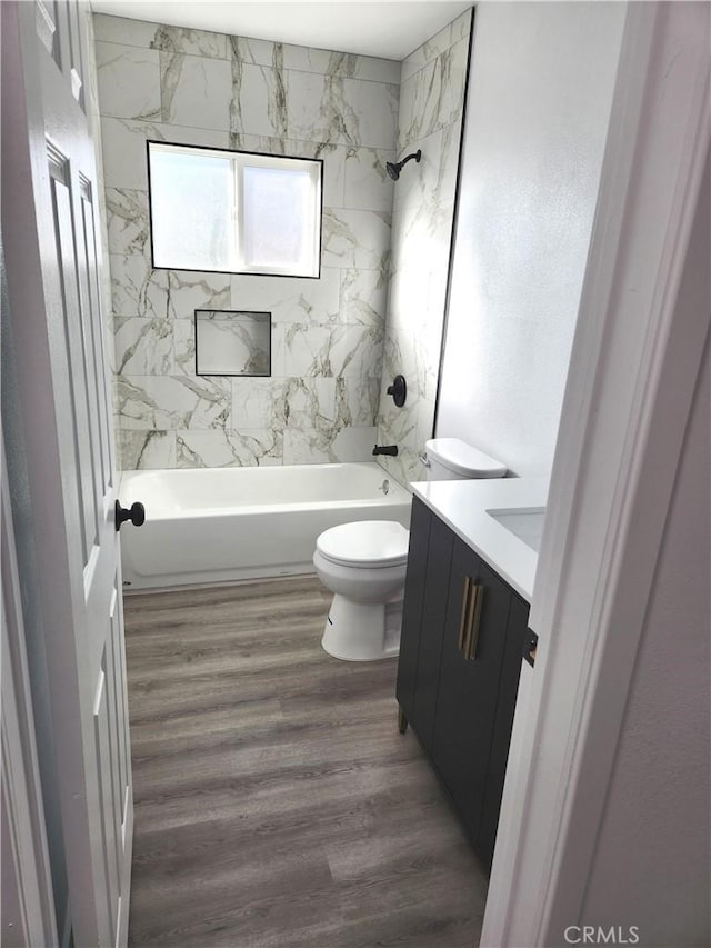 full bathroom featuring hardwood / wood-style flooring, vanity, tiled shower / bath combo, and toilet