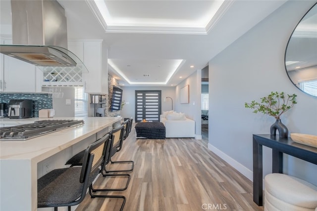 kitchen with a tray ceiling, exhaust hood, white cabinets, light hardwood / wood-style floors, and stainless steel gas stovetop