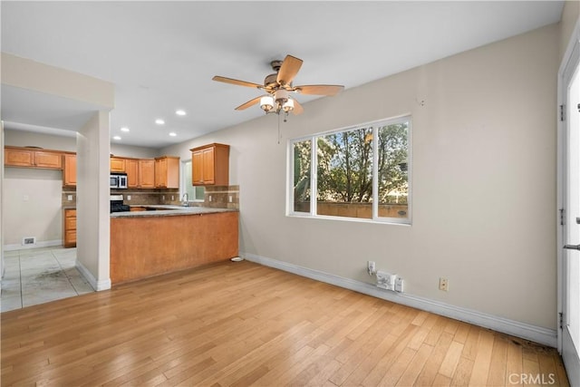 kitchen with backsplash, kitchen peninsula, ceiling fan, and light wood-type flooring