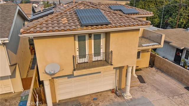 rear view of property featuring a balcony, a garage, and solar panels