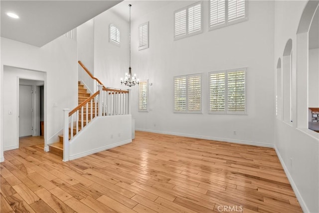 unfurnished living room featuring a notable chandelier, a healthy amount of sunlight, a high ceiling, and light hardwood / wood-style flooring