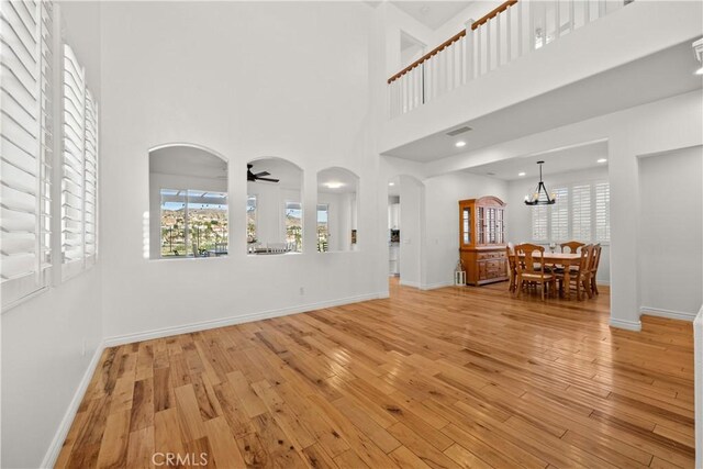 unfurnished living room featuring a high ceiling, ceiling fan with notable chandelier, and light hardwood / wood-style floors