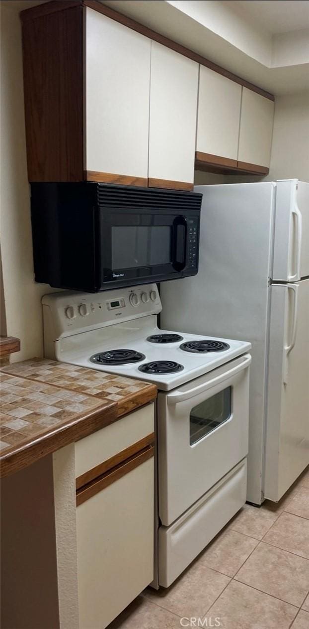 kitchen featuring wood counters, white range with electric cooktop, light tile patterned floors, and white cabinetry