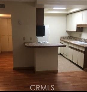 kitchen with kitchen peninsula, sink, white cabinets, and light hardwood / wood-style flooring