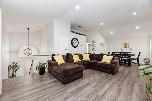 living room featuring a chandelier, light wood-type flooring, and vaulted ceiling