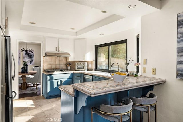 kitchen with stainless steel appliances, a peninsula, a sink, decorative backsplash, and a raised ceiling