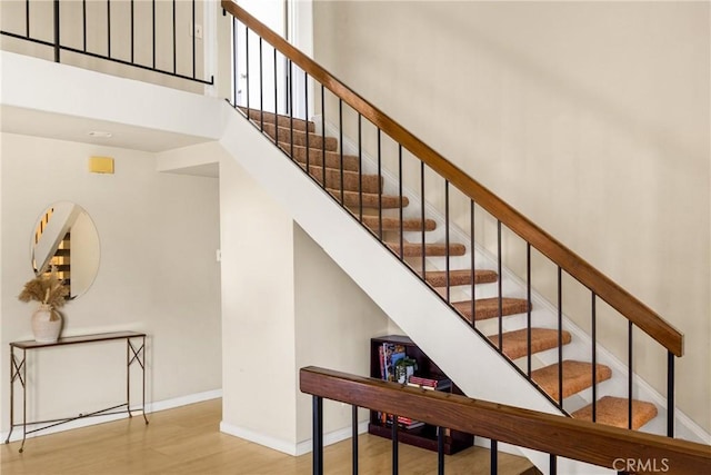 staircase featuring a high ceiling, wood finished floors, and baseboards