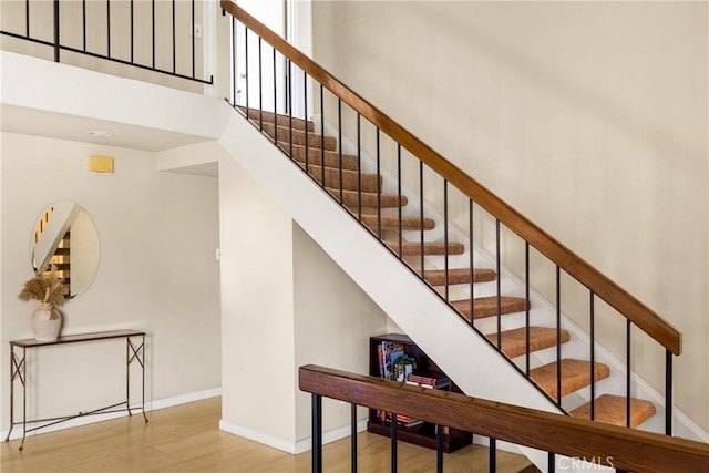 stairs featuring wood finished floors, a high ceiling, and baseboards