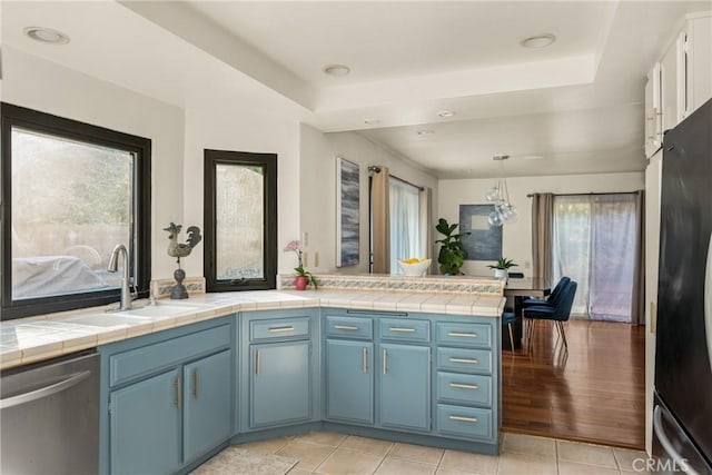 kitchen with blue cabinets, sink, pendant lighting, tile countertops, and dishwasher