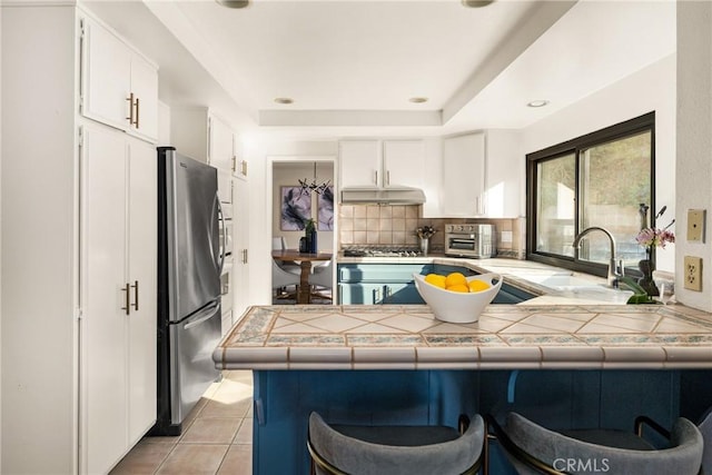 kitchen featuring tile counters, white cabinetry, stainless steel appliances, and kitchen peninsula