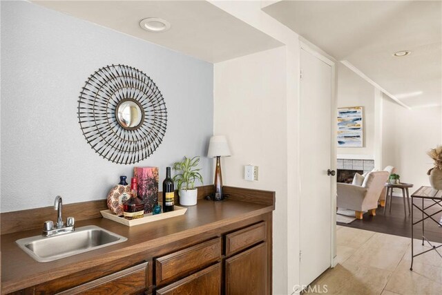 bar with light tile patterned flooring, a tiled fireplace, and sink