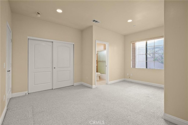 unfurnished bedroom featuring connected bathroom, a closet, and light colored carpet