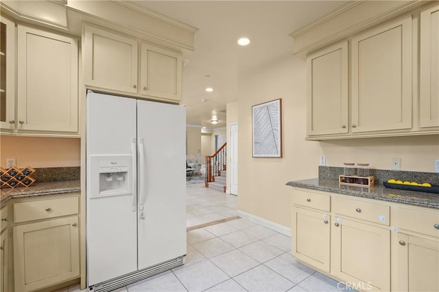 kitchen with dark stone counters, cream cabinets, and white fridge with ice dispenser