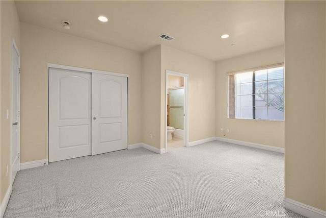 unfurnished bedroom with light colored carpet, ensuite bathroom, and a closet