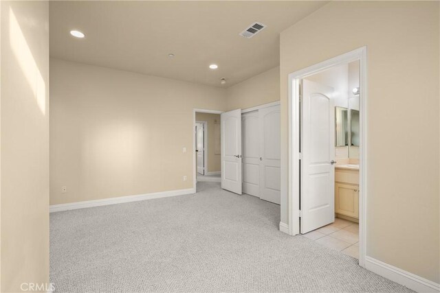 unfurnished bedroom with ensuite bath, a closet, and light carpet