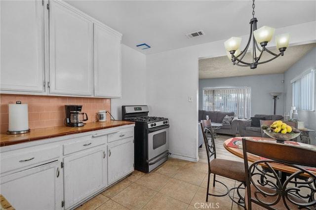 kitchen with decorative backsplash, pendant lighting, white cabinetry, and stainless steel gas range