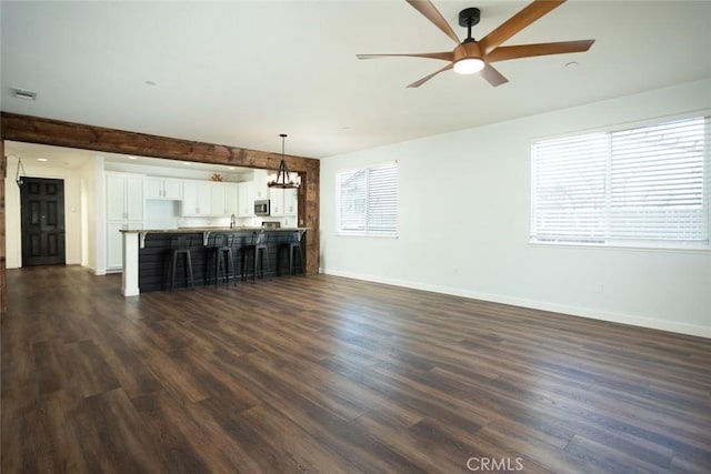 unfurnished living room featuring beam ceiling, dark hardwood / wood-style flooring, and ceiling fan with notable chandelier