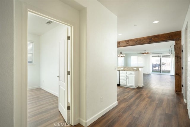 corridor featuring dark hardwood / wood-style floors, beam ceiling, and an inviting chandelier