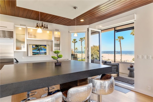 dining room featuring wood finished floors, a beach view, wood ceiling, and a water view