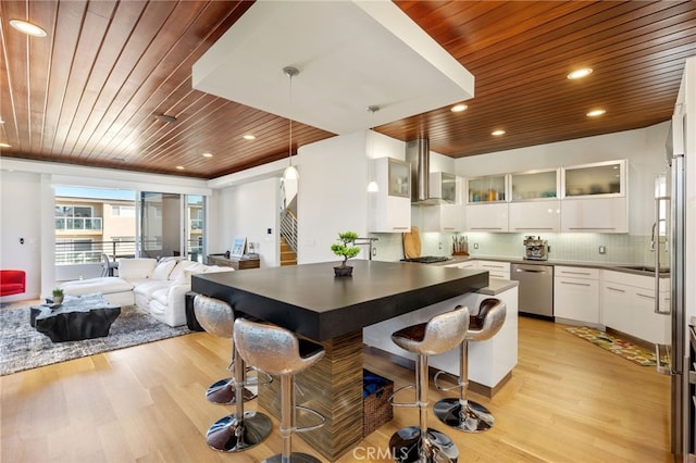 kitchen featuring stainless steel dishwasher, wood ceiling, light wood-style flooring, and wall chimney range hood