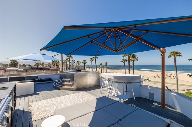 view of patio / terrace featuring a deck with water view, a view of the beach, and a hot tub